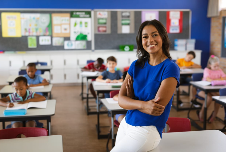 Maestra afroamericana sonriendo en un aula escolar con estudiantes al fondo
