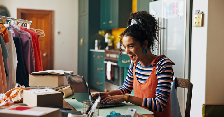 Pequeño empresario gestionando inventario desde casa, rodeado de paquetes y ropa en un espacio de trabajo en la cocina.